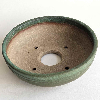 A round ceramic bonsai pot with a textured green glaze on the exterior and a matte brown interior, featuring a drainage hole in the center and four small drainage holes around the rim.