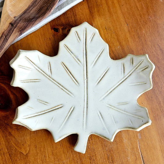 Close-up of handmade cream maple leaf ceramic spoon rest on wooden surface showing glaze detail