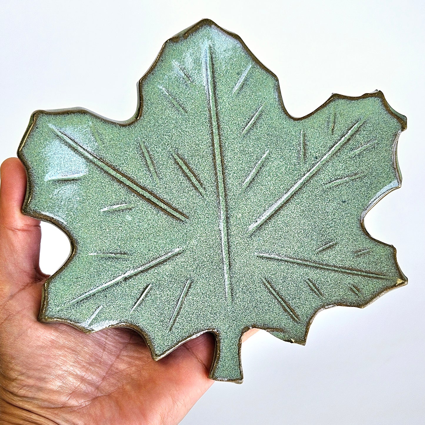 Handmade ceramic maple leaf spoon rest in hand showing glaze texture and leaf details