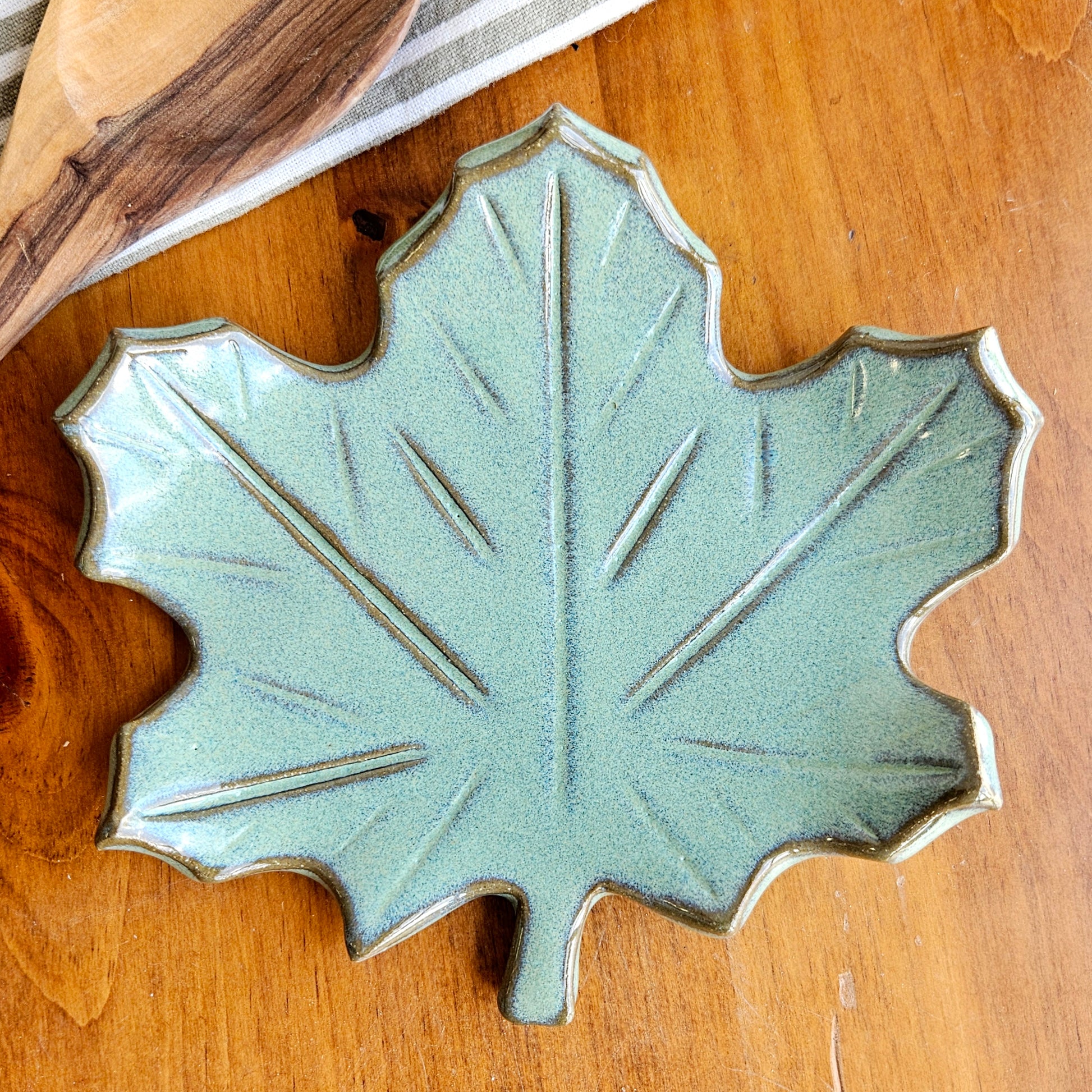 Handmade maple leaf spoon rest in soft green glaze on wood surface beside wooden spoon