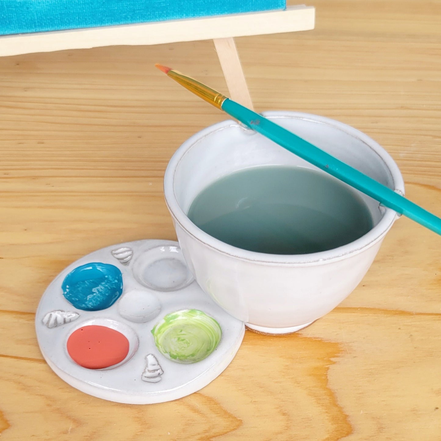 Minimal all-white ceramic paint palette shown in artist’s hand beside a white rinse bowl and watercolor paints.