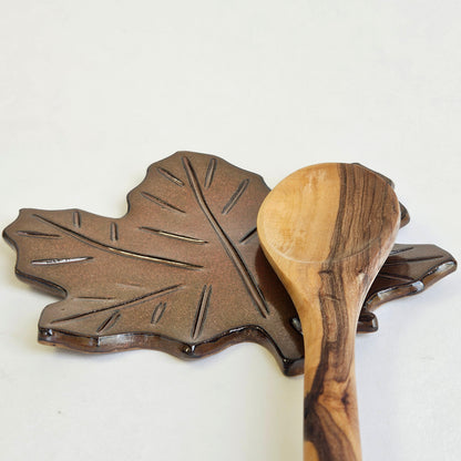 Side view of rust maple leaf spoon rest surrounded by wooden utensils on kitchen counter – rustic fall pottery