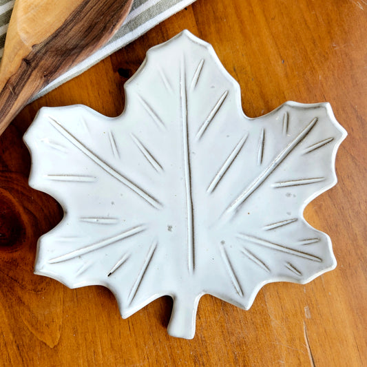 Close-up of handmade white ceramic maple leaf spoon rest on wooden table showing glaze texture and leaf vein detail