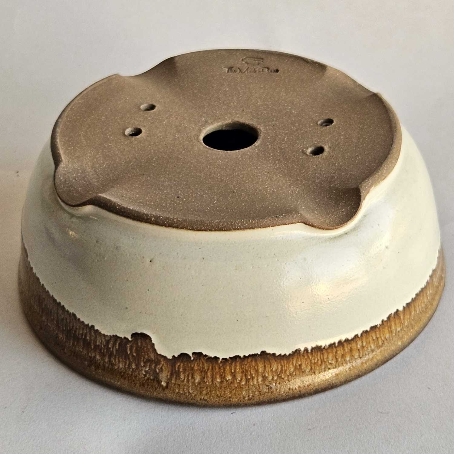 Bottom of a round shohin bonsai pot showing one drainage hole, four tie-down holes, and indented feet.