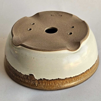 Bottom of a round shohin bonsai pot showing one drainage hole, four tie-down holes, and indented feet.