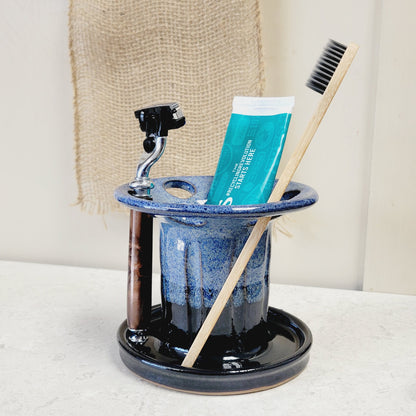A ceramic countertop razor holder with 6 slots, featuring a black and blue striped pattern, with toothbrushes and toothpaste tubes arranged within it.