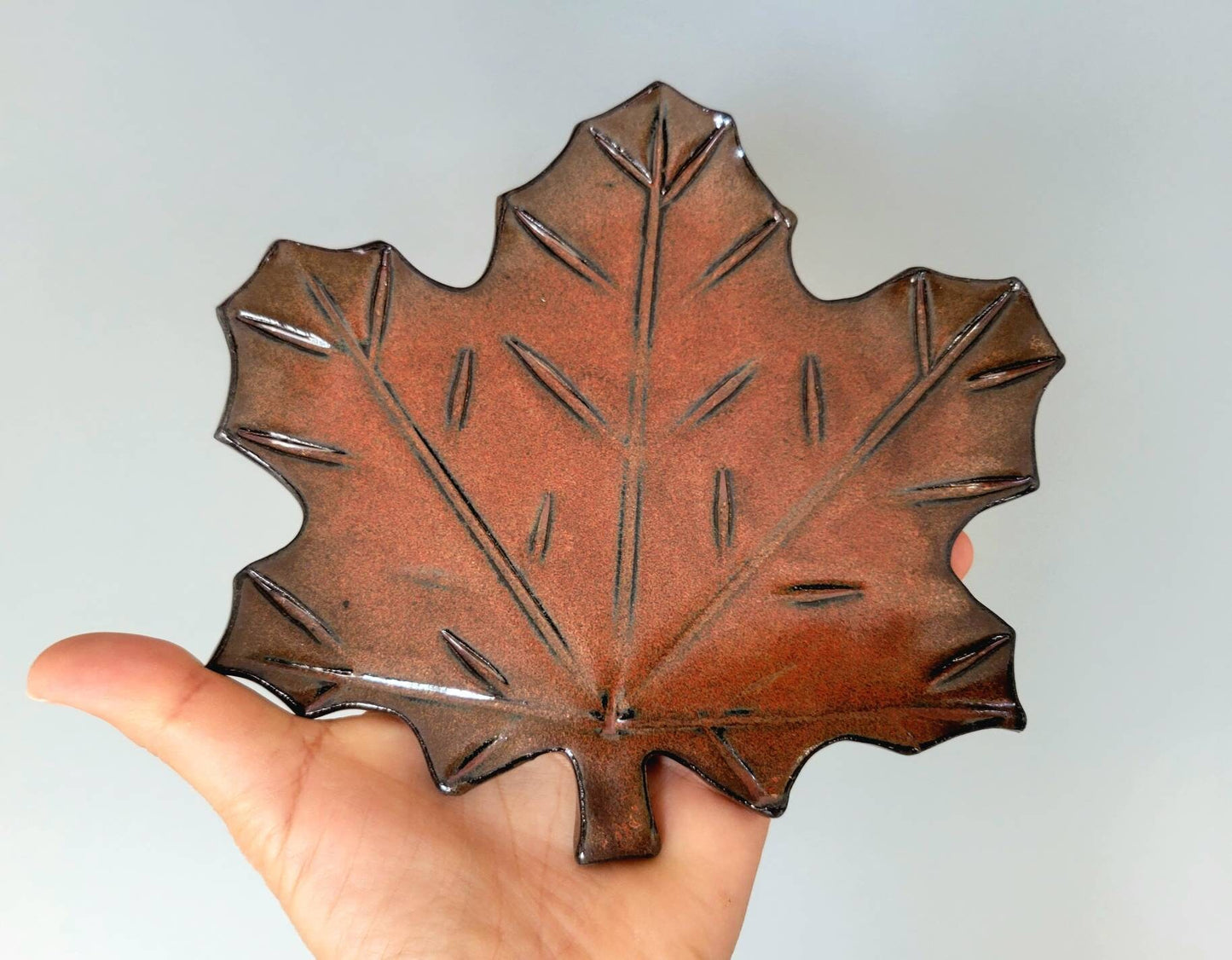 Hand holding handmade rust maple leaf ceramic spoon rest showing natural texture and glaze details